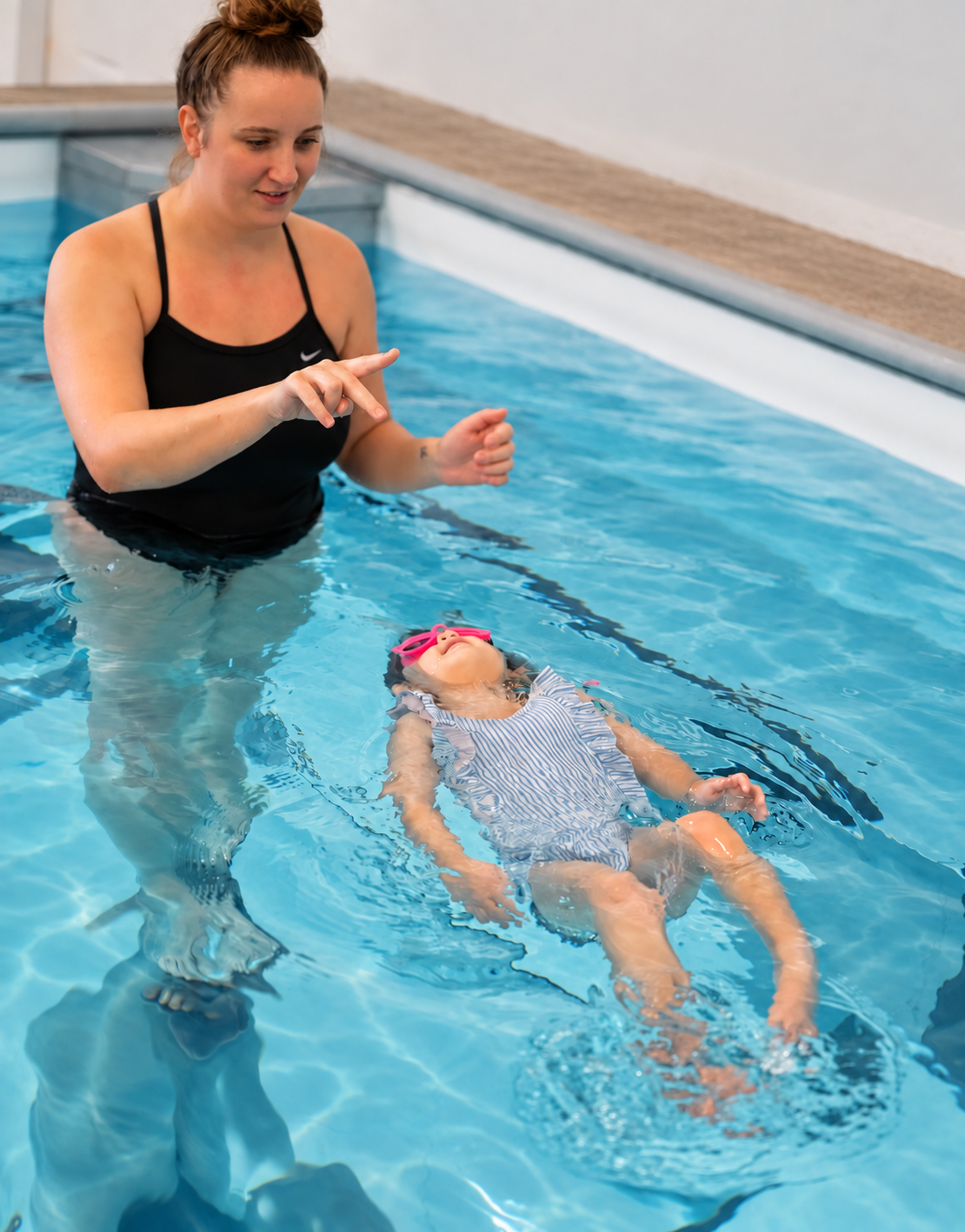 A young swimmer practicing a back float with an instructor